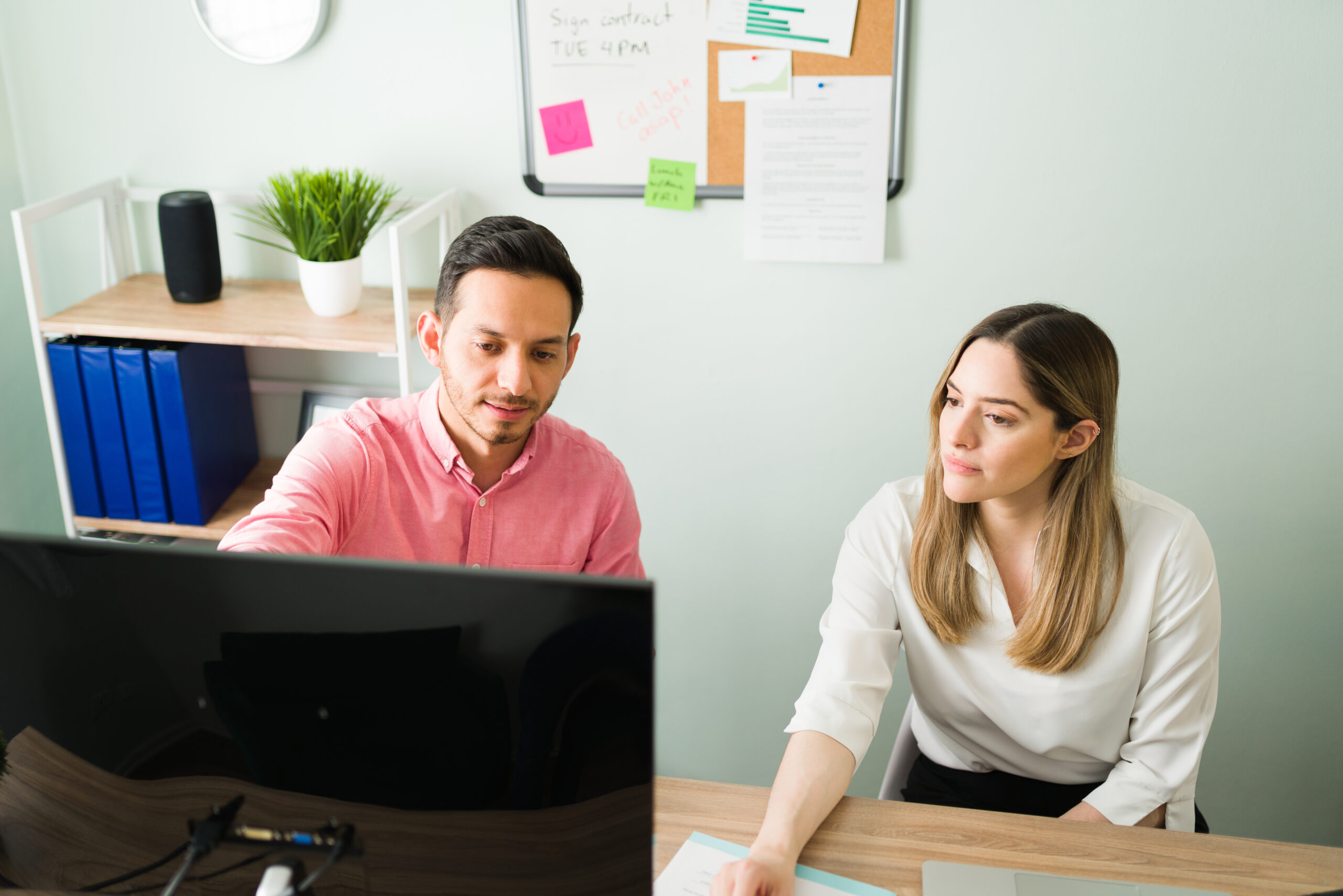 Hispanic man pointing and talking about a business presentation on the computer to his female coworker in the office