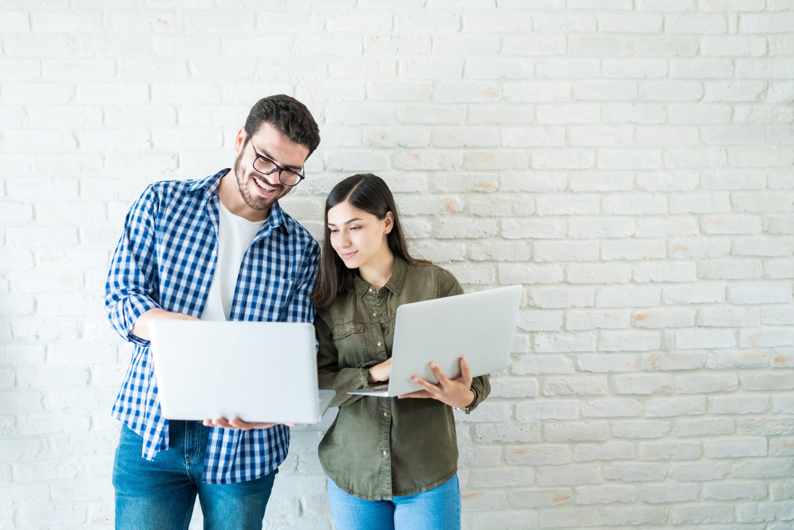 Professional business partners working on laptops while standing against white wall in workplace