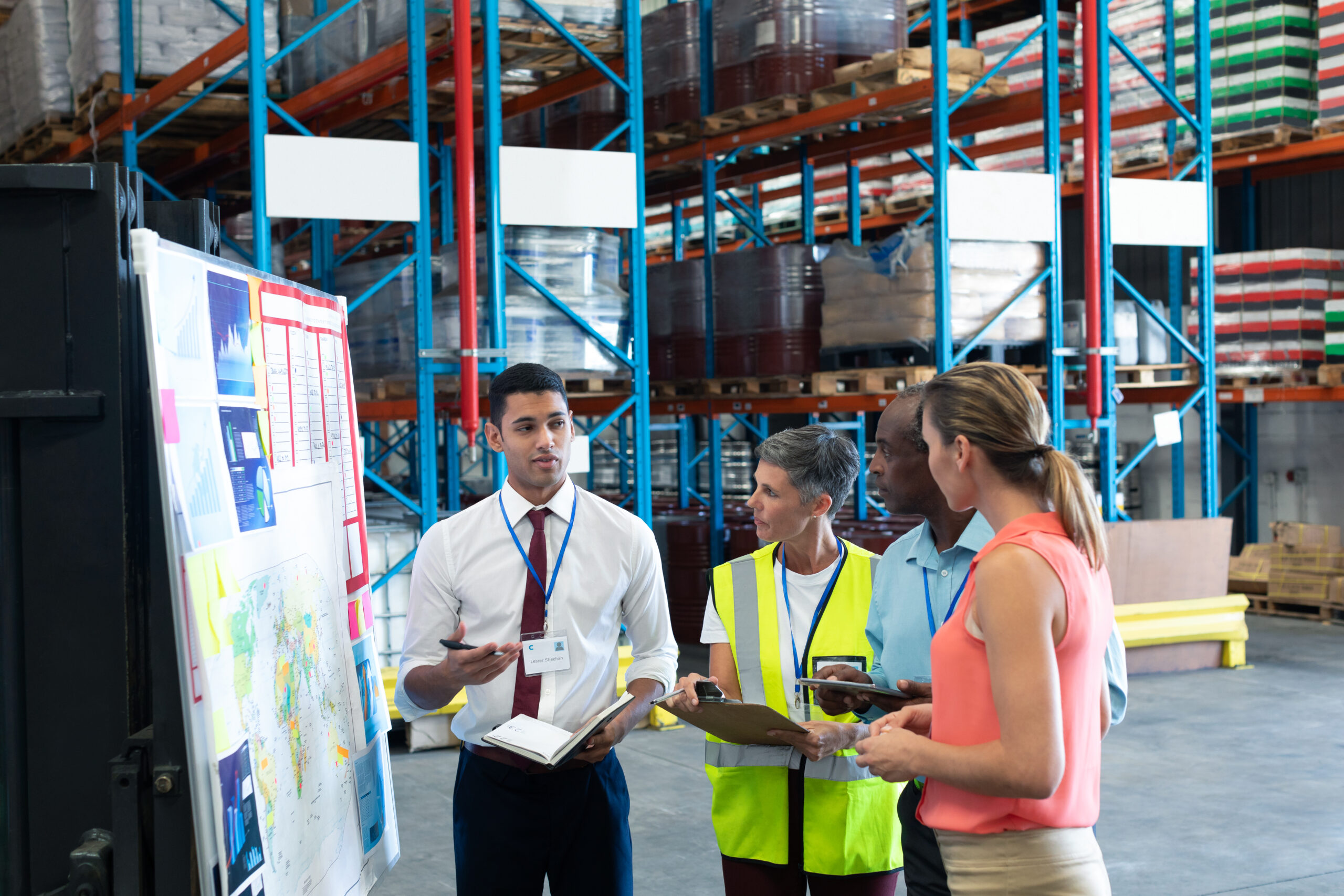 Front view of diverse warehouse staffs discussing over whiteboard in warehouse. This is a freight transportation and distribution warehouse. Industrial and industrial workers concept
